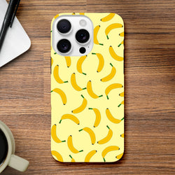 Yellow banana patterned tough iPhone case on a wooden desk. Cute fruit phone cover with playful energy and secure screen protection.