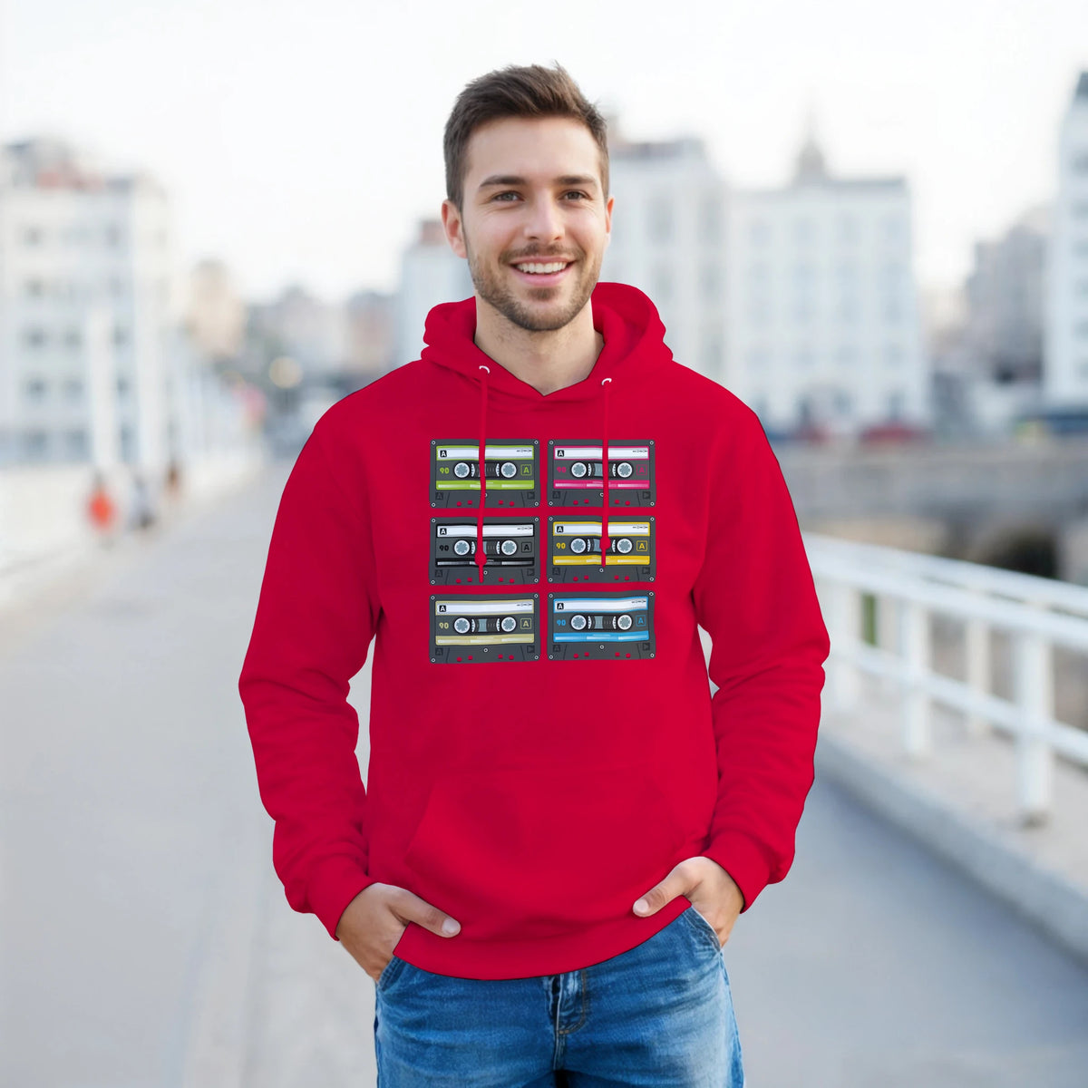 Smiling man in a red retro cassette tape hoodie with a grid of colorful cassette designs.