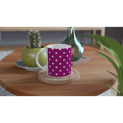 Retro purple and white polka dot ceramic coffee mug sitting on a wooden coaster next to a small potted cactus.