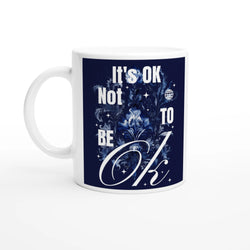 White ceramic mug with navy blue graphic reading It's OK Not To Be OK, surrounded by floral design.