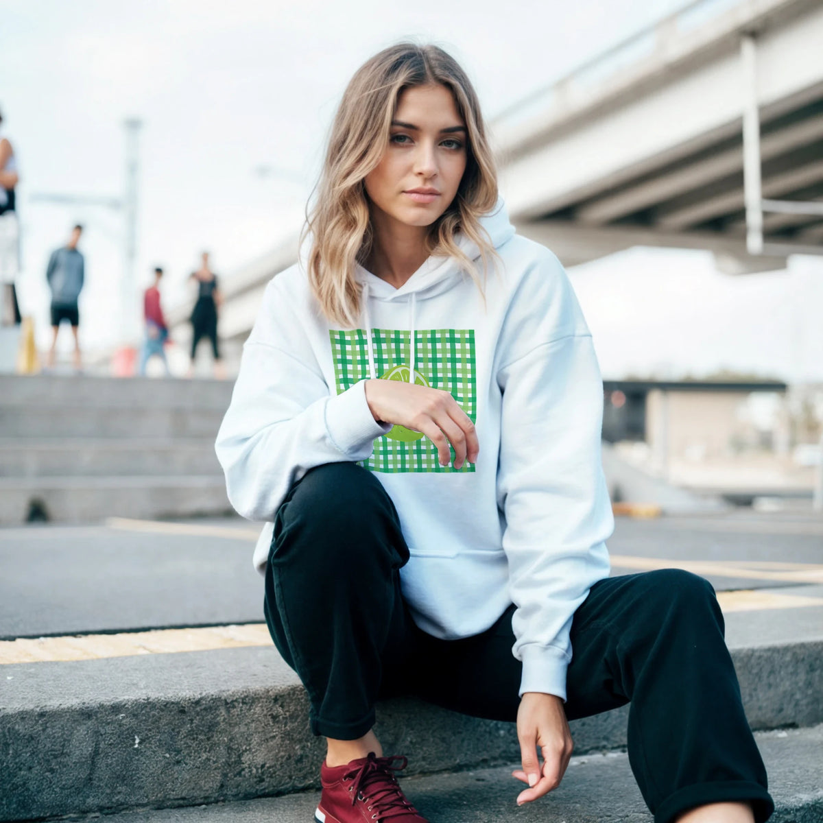 Woman wearing white hooded pullover with retro lime green gingham and fruit graphic, styled with black pants for urban streetwear.