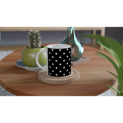 Black and white polka dot ceramic mug on wooden coaster beside cactus and glass vase on table.