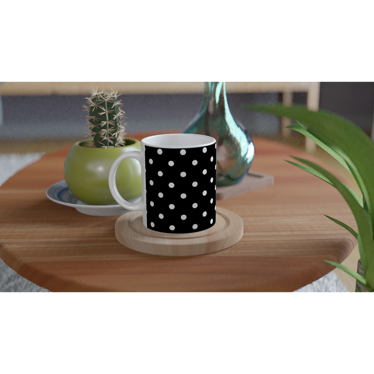 Black and white polka dot ceramic mug on wooden coaster beside cactus and glass vase on table.