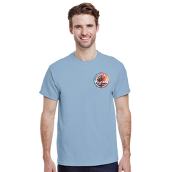 Man wearing light blue t-shirt with circular retro Urban Palm Trees graphic on chest. Casual streetwear top featuring colorful palm tree and mountain design.