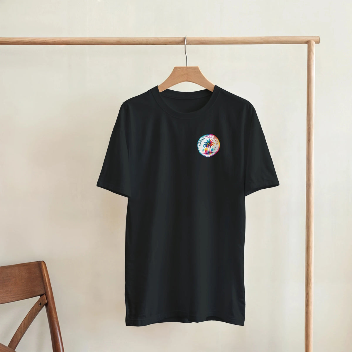 Black retro tee with colorful circular palm tree chest print hanging on wooden rack. Tropical women's short sleeve shirt.
