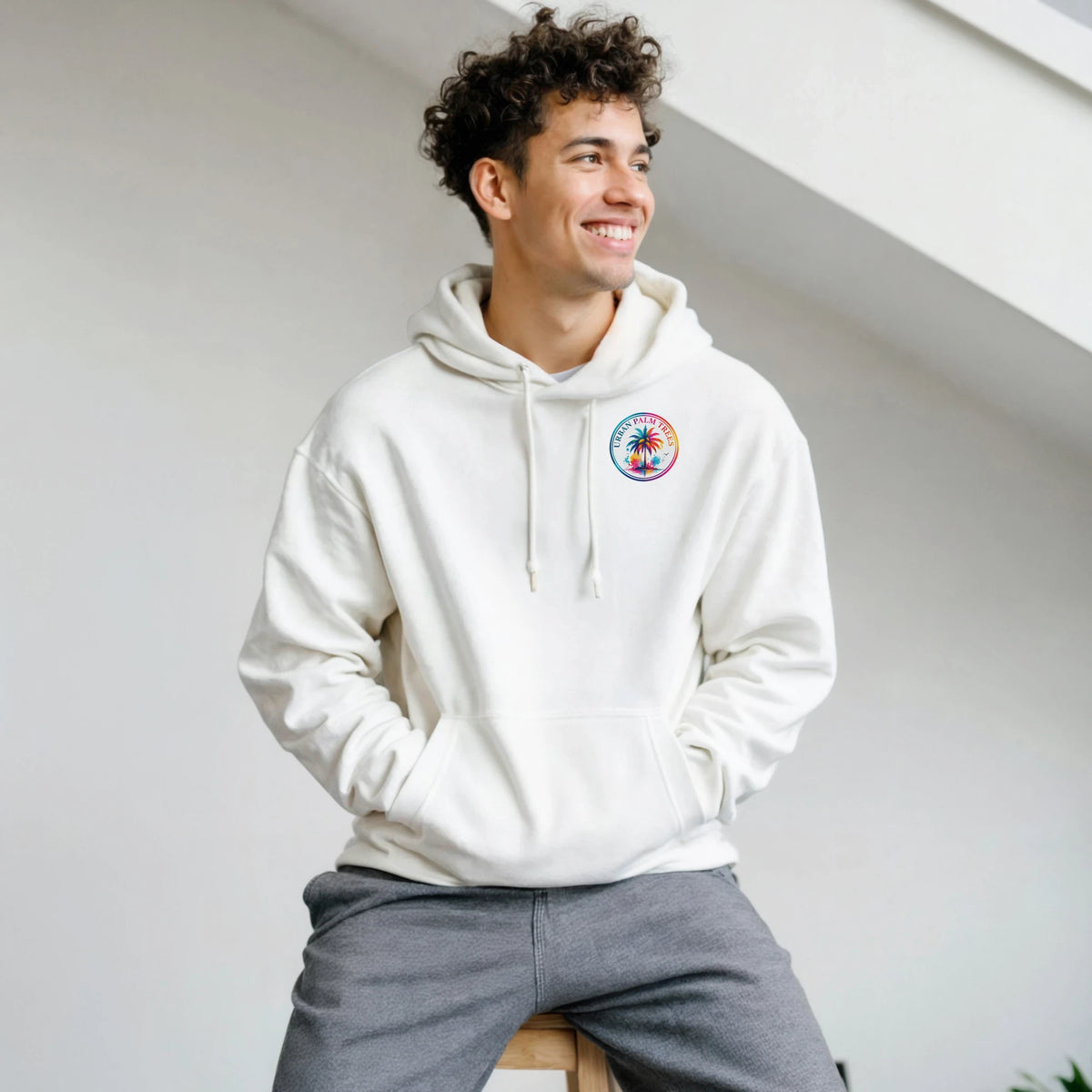 Man wearing white hoodie with colorful circular palm tree chest logo. Casual music-inspired streetwear with double-lined hood and matching drawstrings.