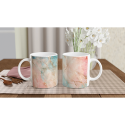 Pastel marble mugs with peach and aqua abstract patterns on a wooden table behind a bouquet of white flowers.
