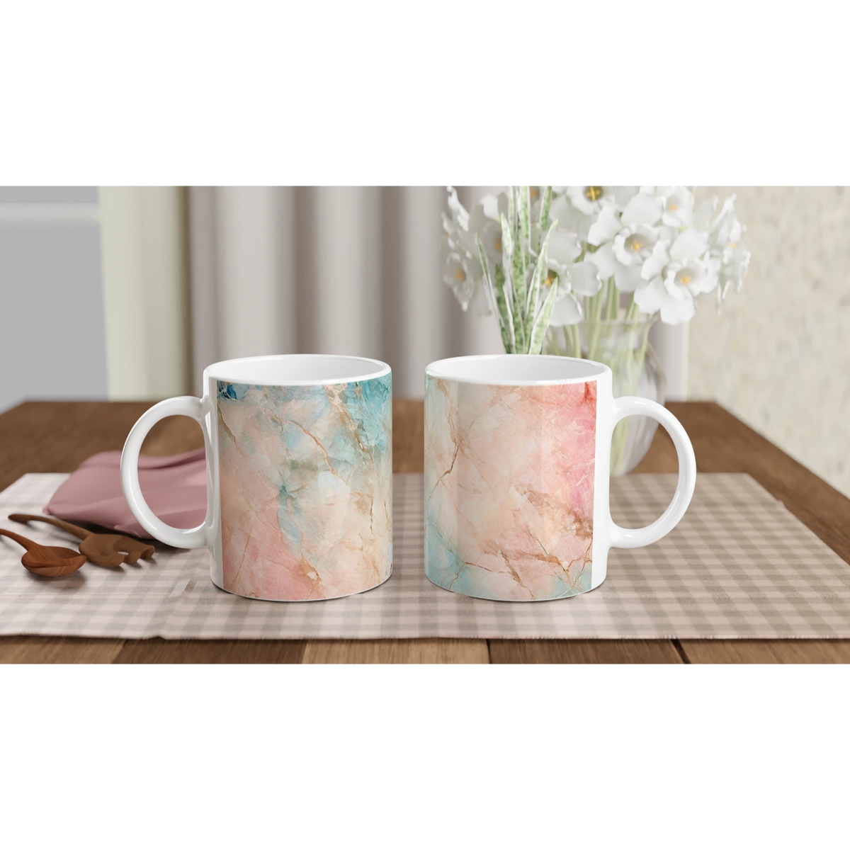 Pastel marble mugs with peach and aqua abstract patterns on a wooden table behind a bouquet of white flowers.