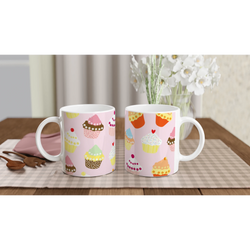 Two pastel pink cupcake mugs with kawaii designs on a checkered table, white flowers in the background.