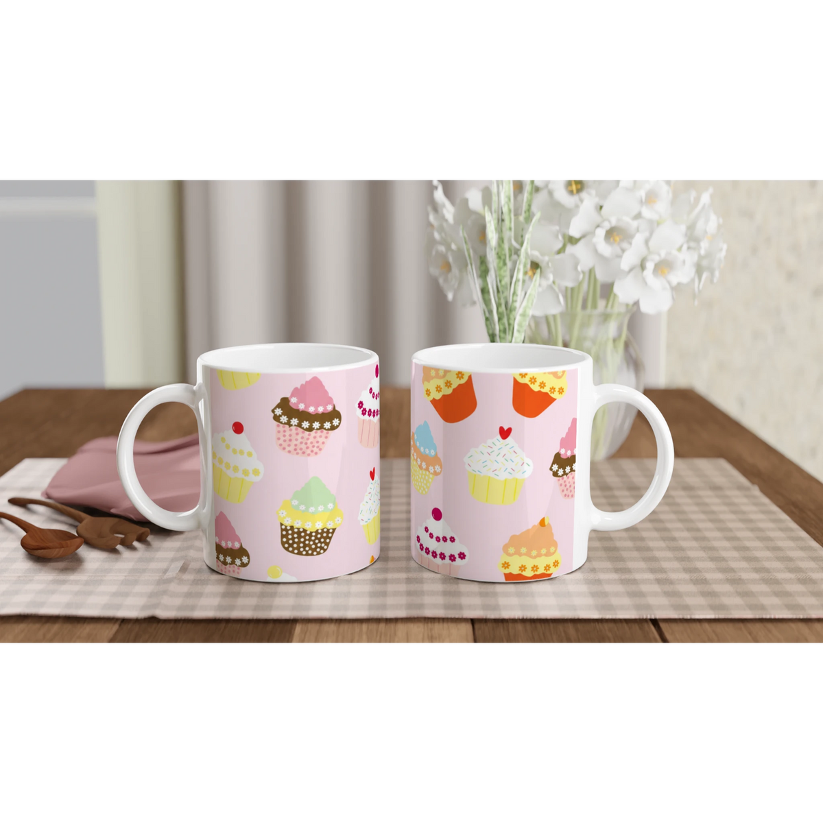 Two pastel pink cupcake mugs with kawaii designs on a checkered table, white flowers in the background.