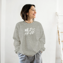 Smiling woman wearing gray Cute Wild And Free Sweatshirt with white slogan, casual streetwear.