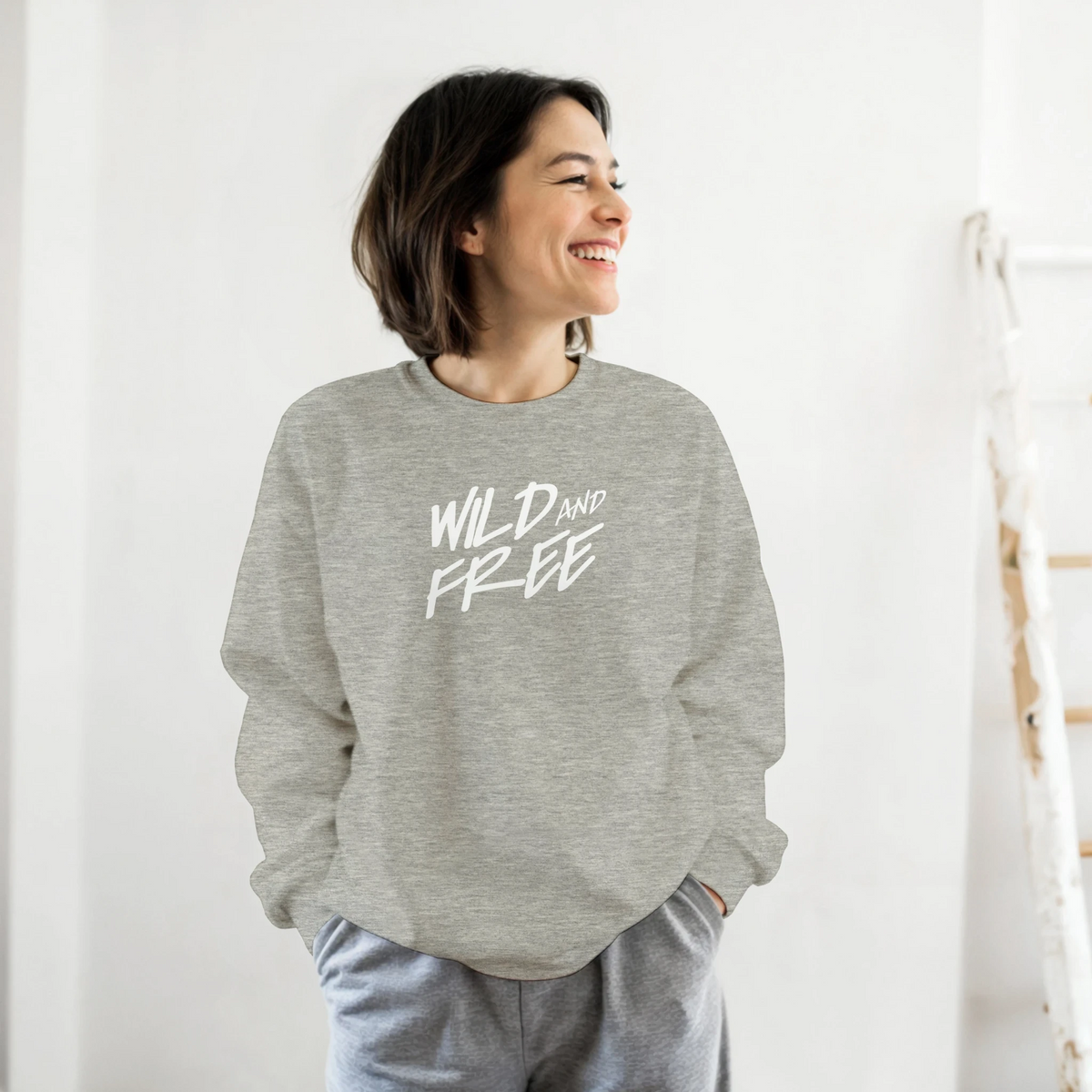 Smiling woman wearing gray Cute Wild And Free Sweatshirt with white slogan, casual streetwear.