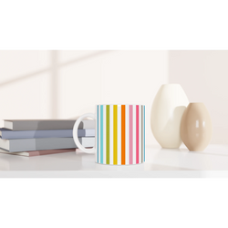Rainbow Stripe Ceramic Mug with vertical multicolor stripes on a white desk, beside stacked books.