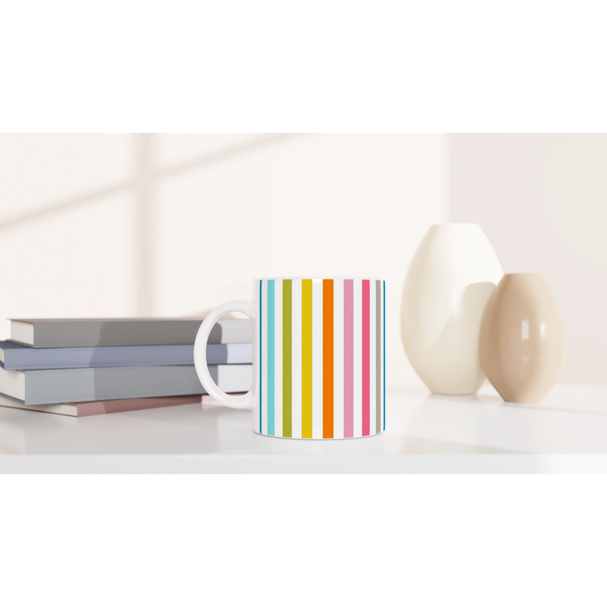 Rainbow Stripe Ceramic Mug with vertical multicolor stripes on a white desk, beside stacked books.