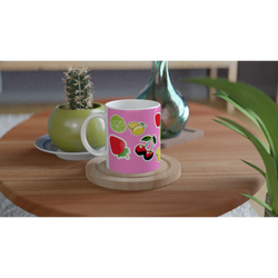 Pink ceramic mug featuring cute cherries, lemons, limes, and strawberries on a wooden table with a cactus.