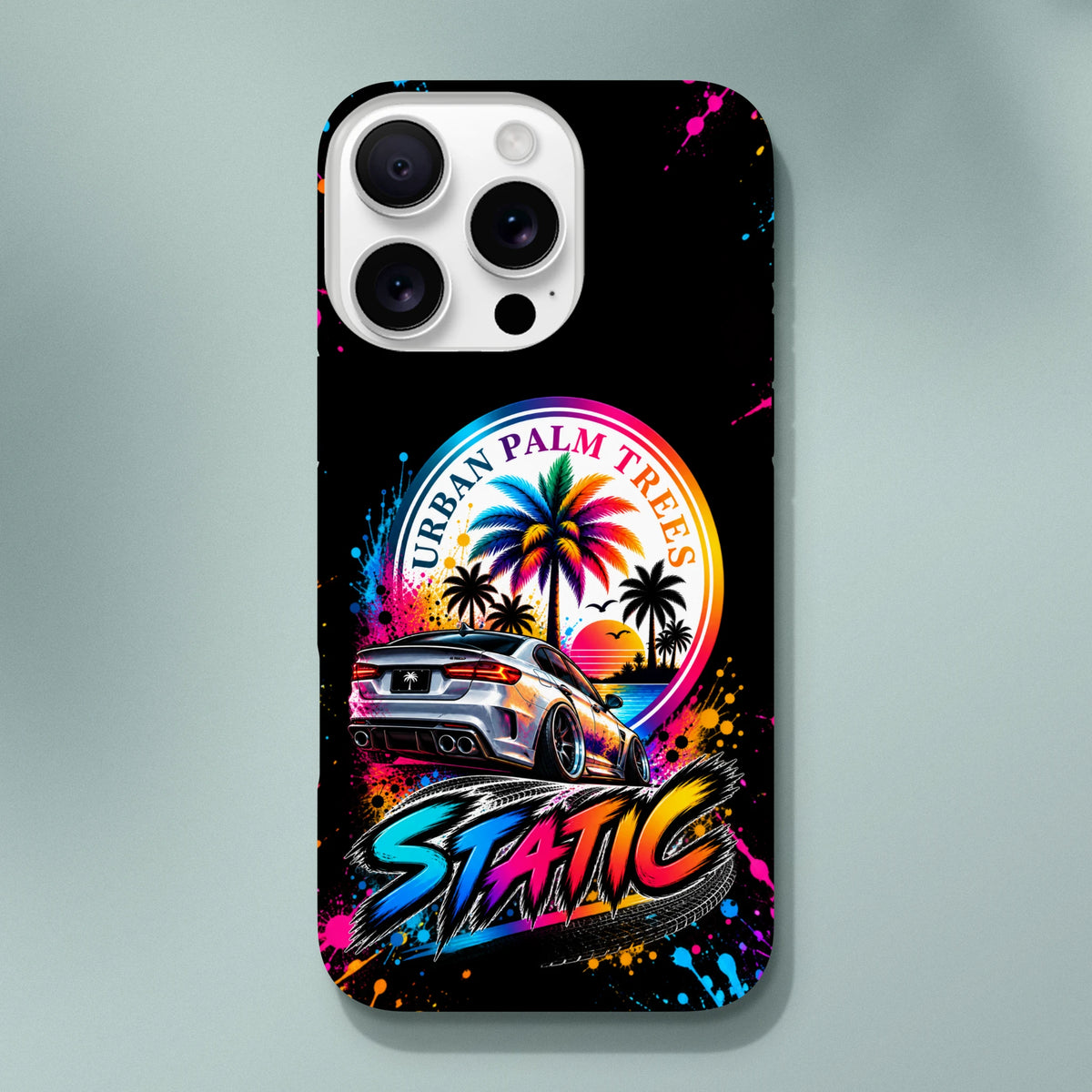 Static Slammed iPhone case featuring a silver modified car, colorful "Urban Palm Trees" sunset, and vibrant paint splatter art.