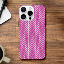 Pink herringbone iPhone case with geometric chevron pattern resting on wood, offering tough impact resistance for daily use.
