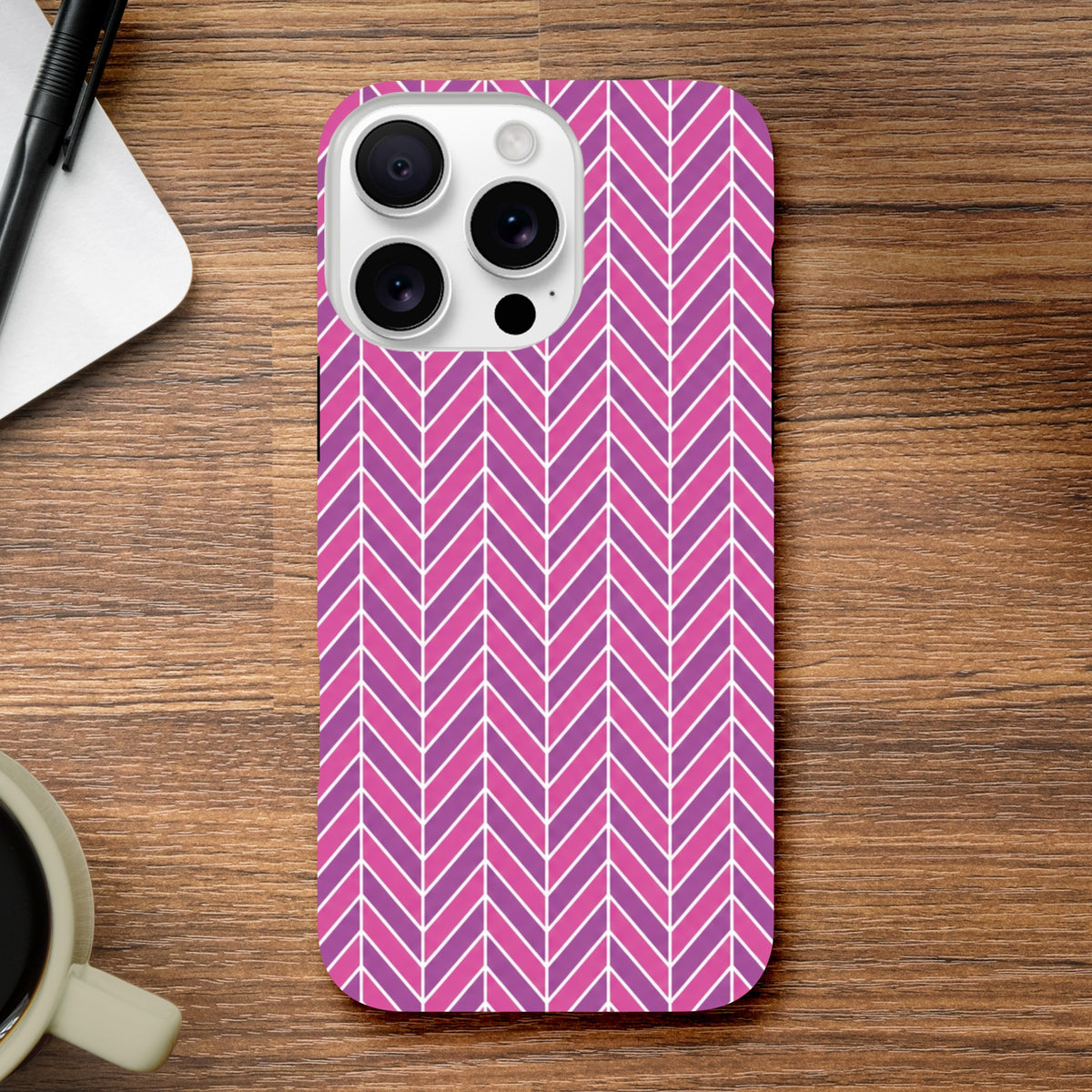 Pink herringbone iPhone case with geometric chevron pattern resting on wood, offering tough impact resistance for daily use.