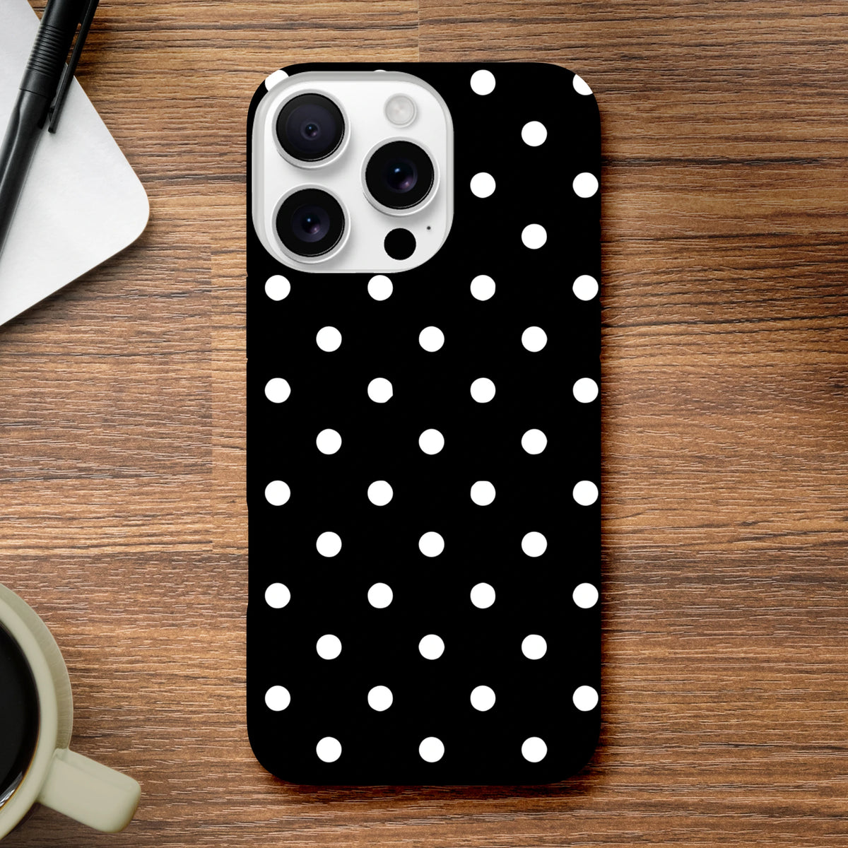 Black and white polka dot tough iPhone Case with vintage style and shock-absorbing protection for models 13-16 on a wooden desk.