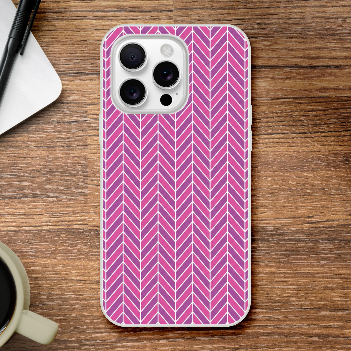 Pink geometric herringbone iPhone case with frosty transparent finish on wooden desk.