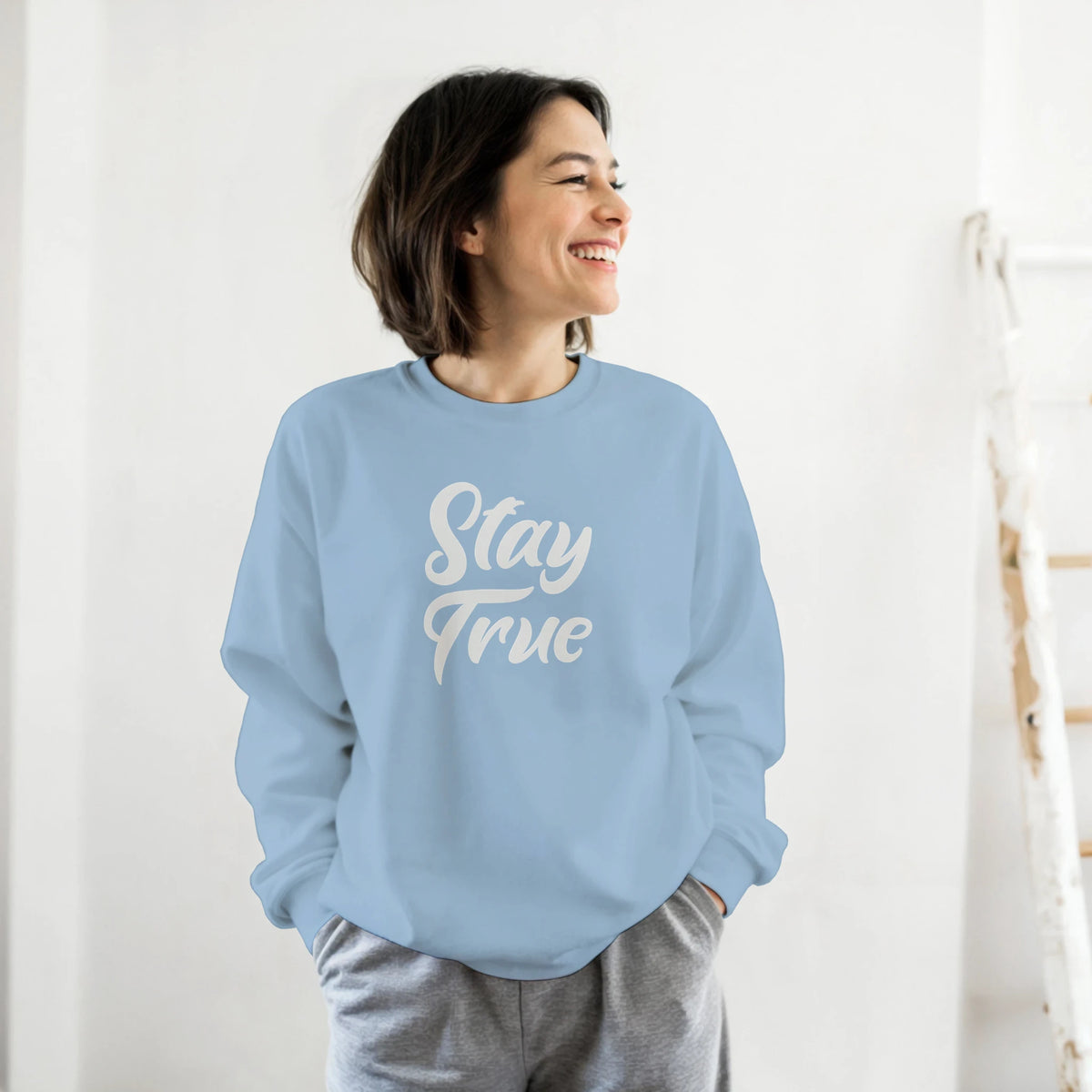 Woman wearing light blue Cute Stay True Sweatshirt, a cozy top for women, smiling indoors.
