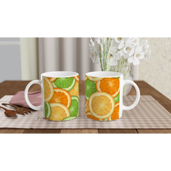 Two citrus-pattern mugs with orange and lime slices on a checkered table near a vase of white flowers.