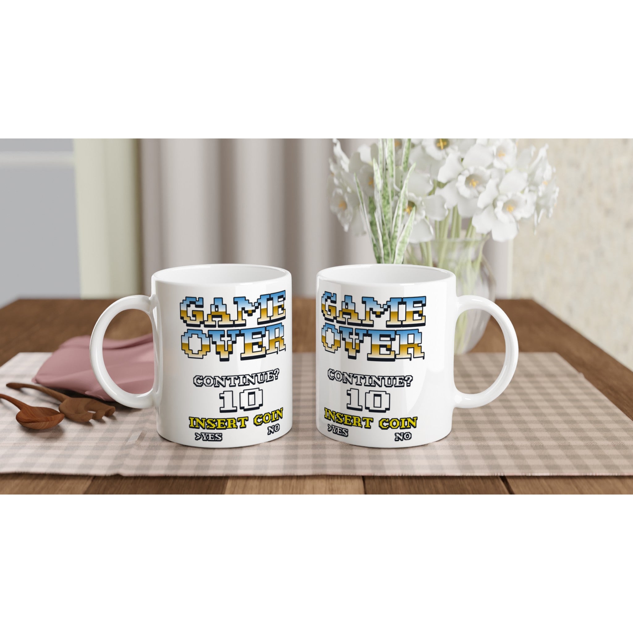 Two white ceramic mugs with retro 90s arcade 'Game Over' print and 'CONTINUE? 10 INSERT COIN' on a wooden table.