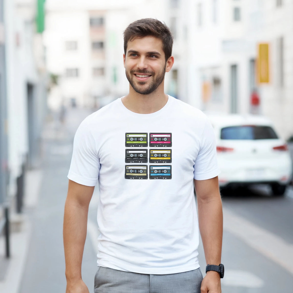 Man wearing white t-shirt with six colorful vintage cassette tape prints, representing retro 80s music nostalgia and streetwear style.