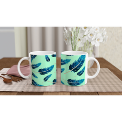 Two mint-green mugs with blue feather patterns on a checkered table, white flowers in the background.