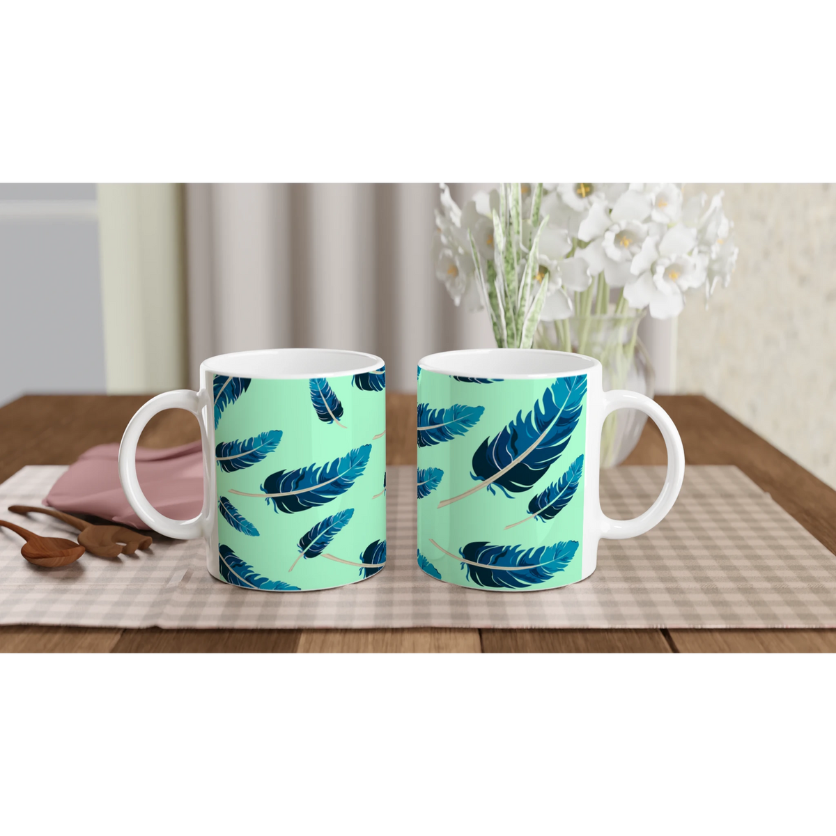 Two mint-green mugs with blue feather patterns on a checkered table, white flowers in the background.