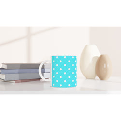 Aqua blue ceramic mug with white polka dots sits on a white desk next to stacked books and small vases.