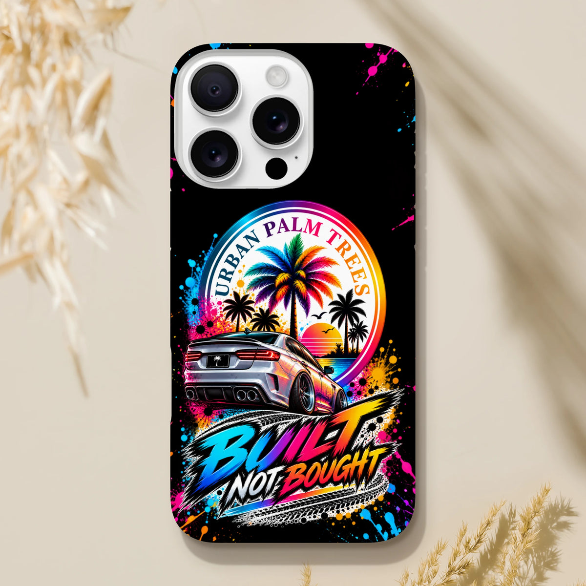 Built Not Bought iPhone case featuring a modified car, colorful Urban Palm Trees sunset graphic, and vibrant paint splatter art on a black background.