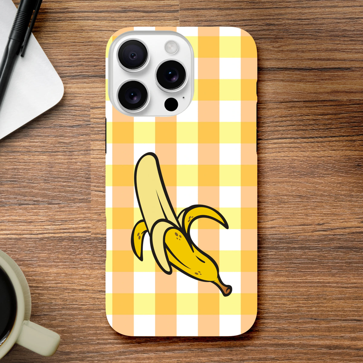 Yellow gingham iPhone case featuring a cute peeled banana illustration on a wood desk.