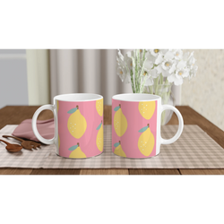 Two pink ceramic mugs with yellow lemon pattern on a checkered tablecloth and a floral vase in the background.