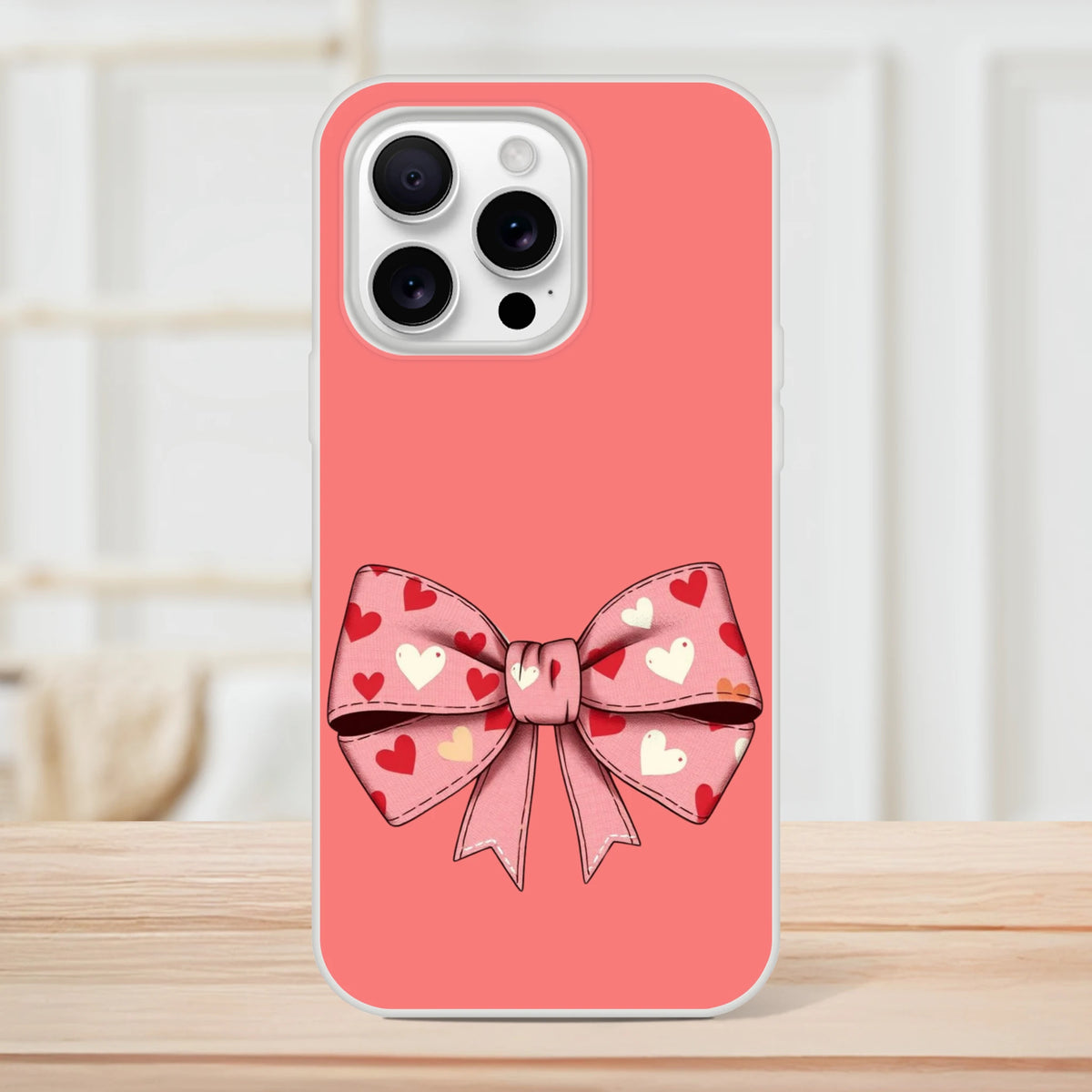 Pink iPhone case with a large heart-patterned bow on the back for iPhone 13–16, camera cutout visible.