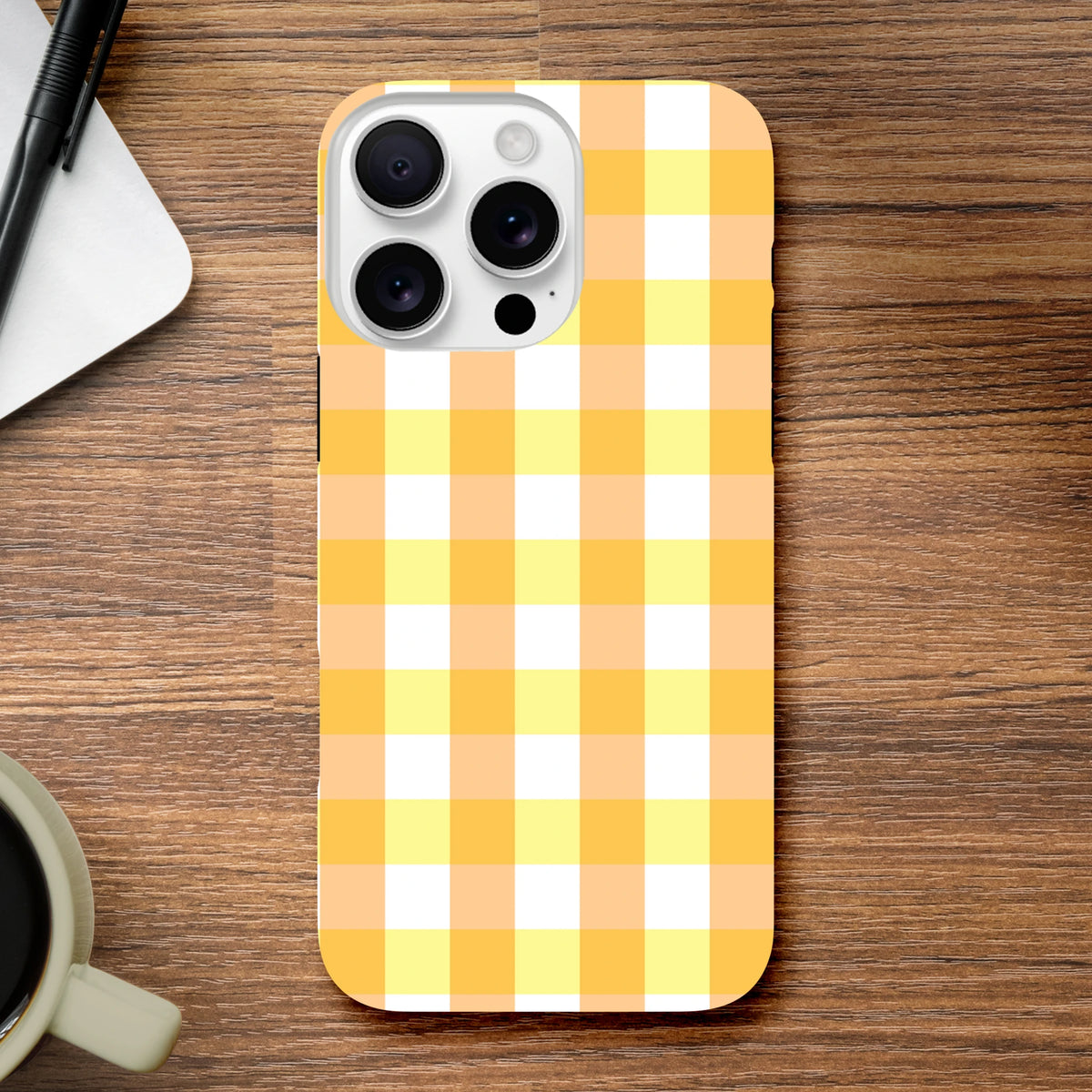 Retro yellow gingham checkered iPhone case on wooden desk. Cute protective cover featuring a bold orange, yellow, and white wraparound grid pattern for urban style.