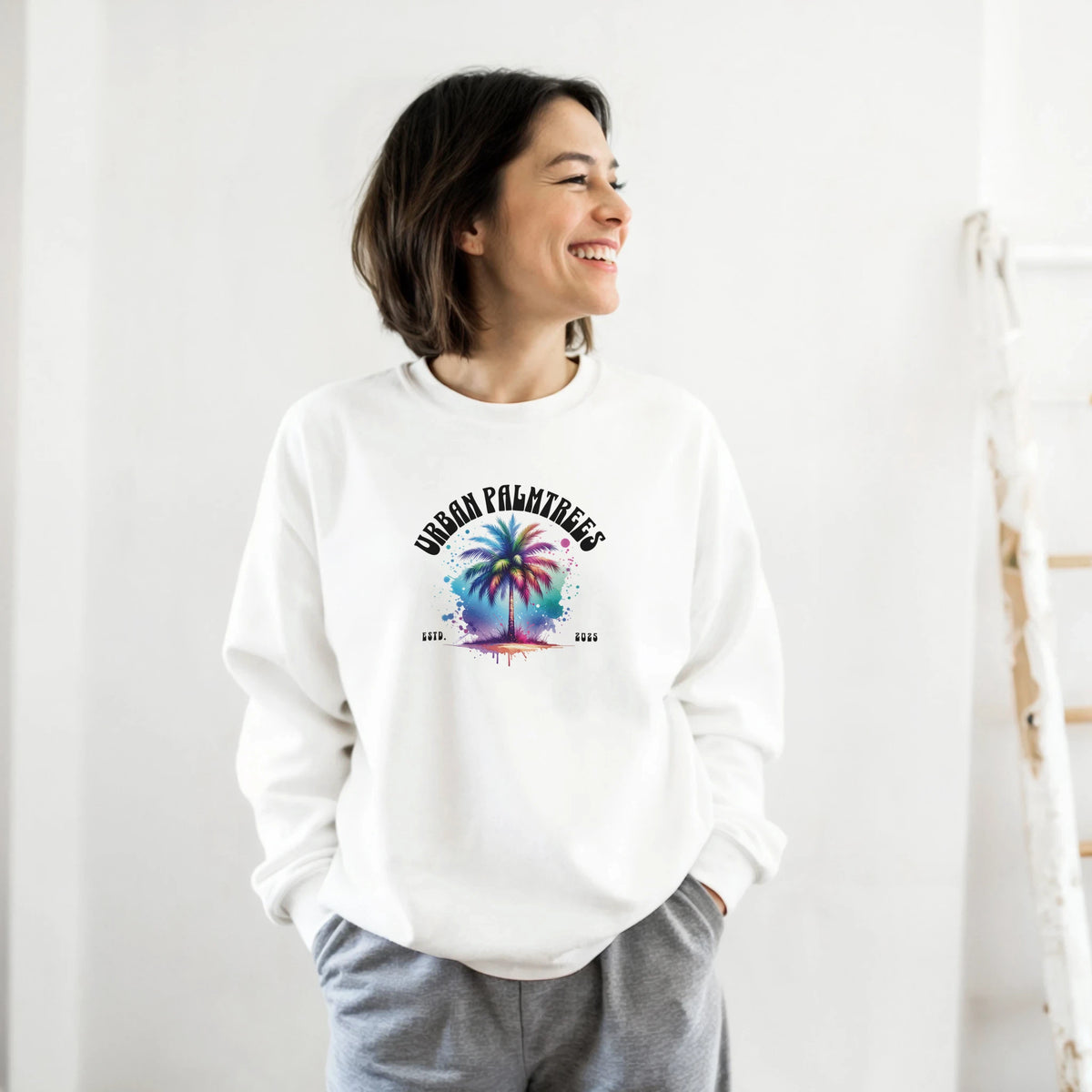 Woman wearing a white Urban Palm Trees sweatshirt with a pastel palm tree graphic.