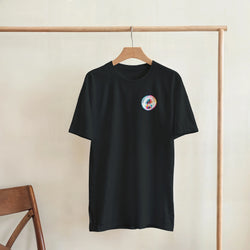Black crew neck t-shirt featuring a retro colorful Urban Palm Trees logo on the chest, hanging on a wooden rack.