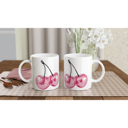 Three white mugs with glitter pink cherries design on a checkered table, white flowers in the background.