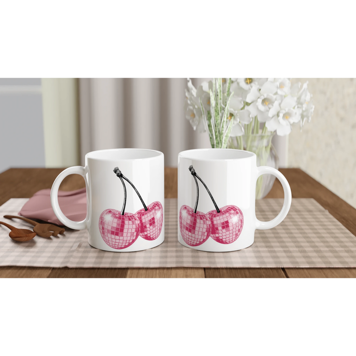 Three white mugs with glitter pink cherries design on a checkered table, white flowers in the background.