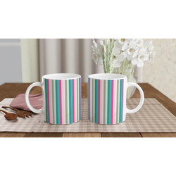 Pastel rainbow stripe ceramic mugs on a table, cute colorful coffee cups with white flowers in the background.