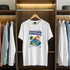 White t-shirt with 'Tropical Paradise' design hanging in a wardrobe with other clothes.