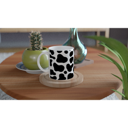 Cow-print black-and-white ceramic mug on a wooden table with plants nearby.