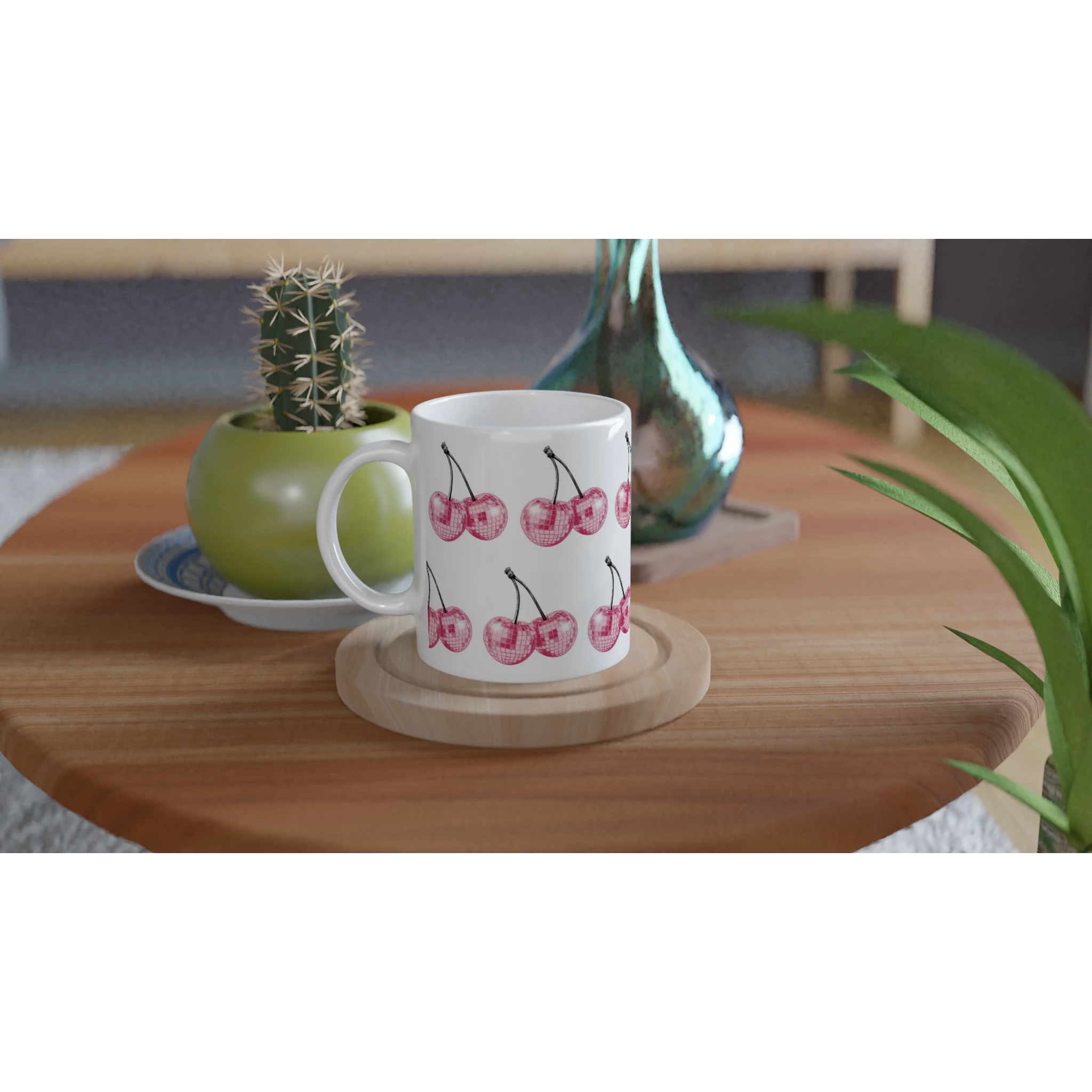 Glitter Ball Cherries mug with pink cherry print on white ceramic, placed on a wooden coaster beside plants.