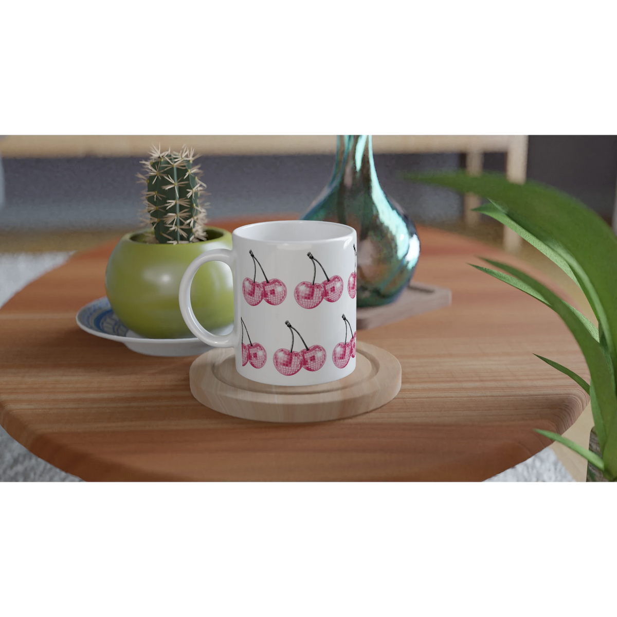 Glitter Ball Cherries mug with pink cherry print on white ceramic, placed on a wooden coaster beside plants.