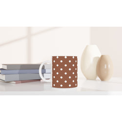 Retro brown ceramic mug with white polka dots on a white desk beside stacked books and minimalist vases.