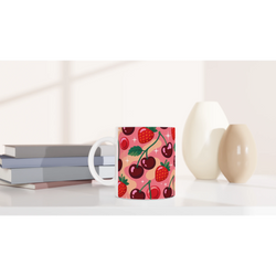 Retro cherry and strawberry pattern ceramic mug on a white desk beside books and vases.