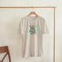 Paradise tropical floral graphic tee on beige cotton blend, short sleeve crew neck, sizes S–XL.