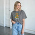 Smiling woman wearing a grey Fresh Juice graphic T-shirt featuring a juice carton and citrus fruits.