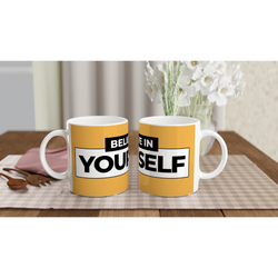 Pair of yellow Believe Yourself mugs with bold slogan text on a wooden table near a vase of white flowers.